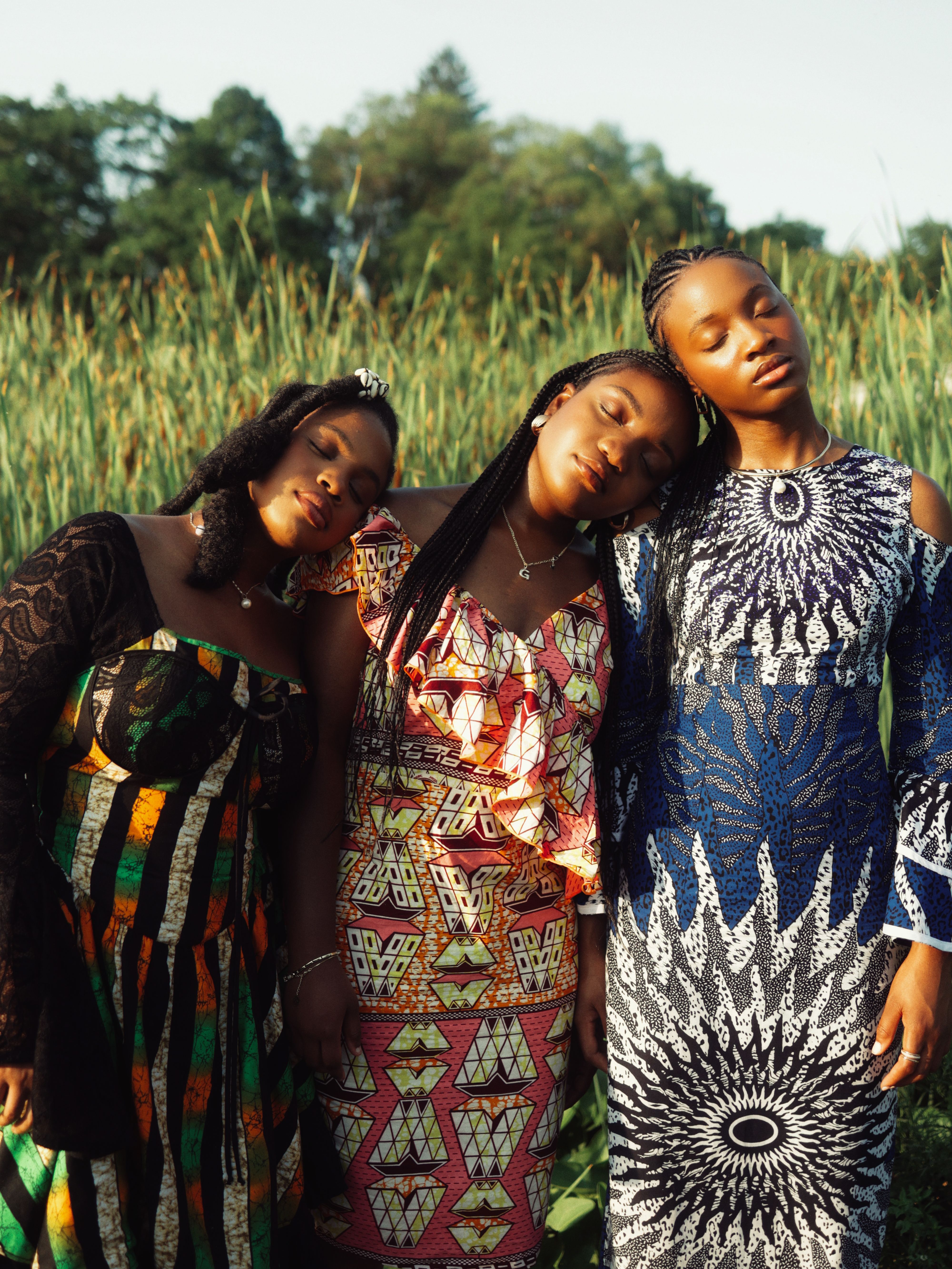 Three women in colorful traditional dresses standing outdoors, embracing a serene moment.