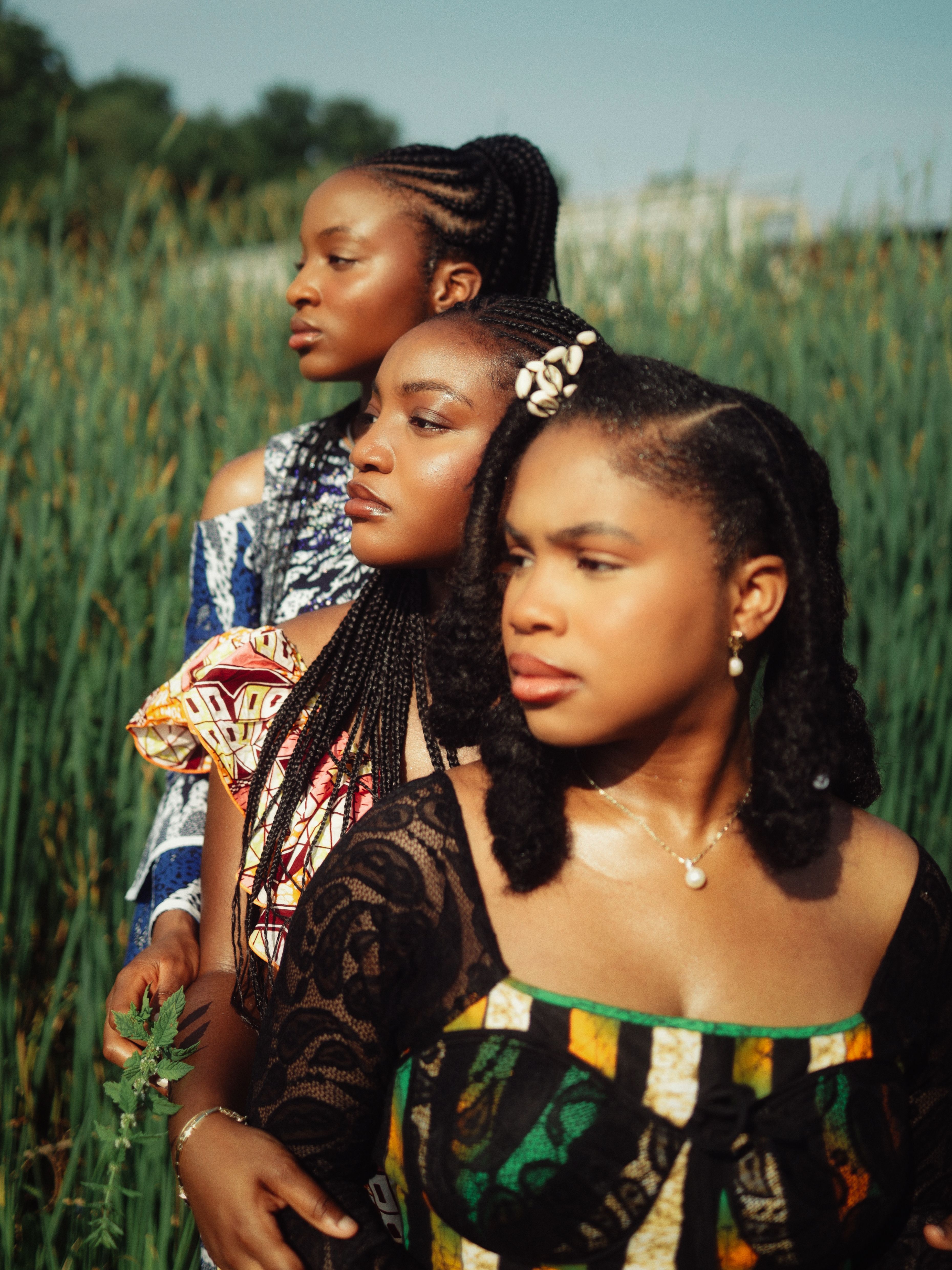 Three women in vibrant African dresses stand in a lush green field, embracing culture and nature.
