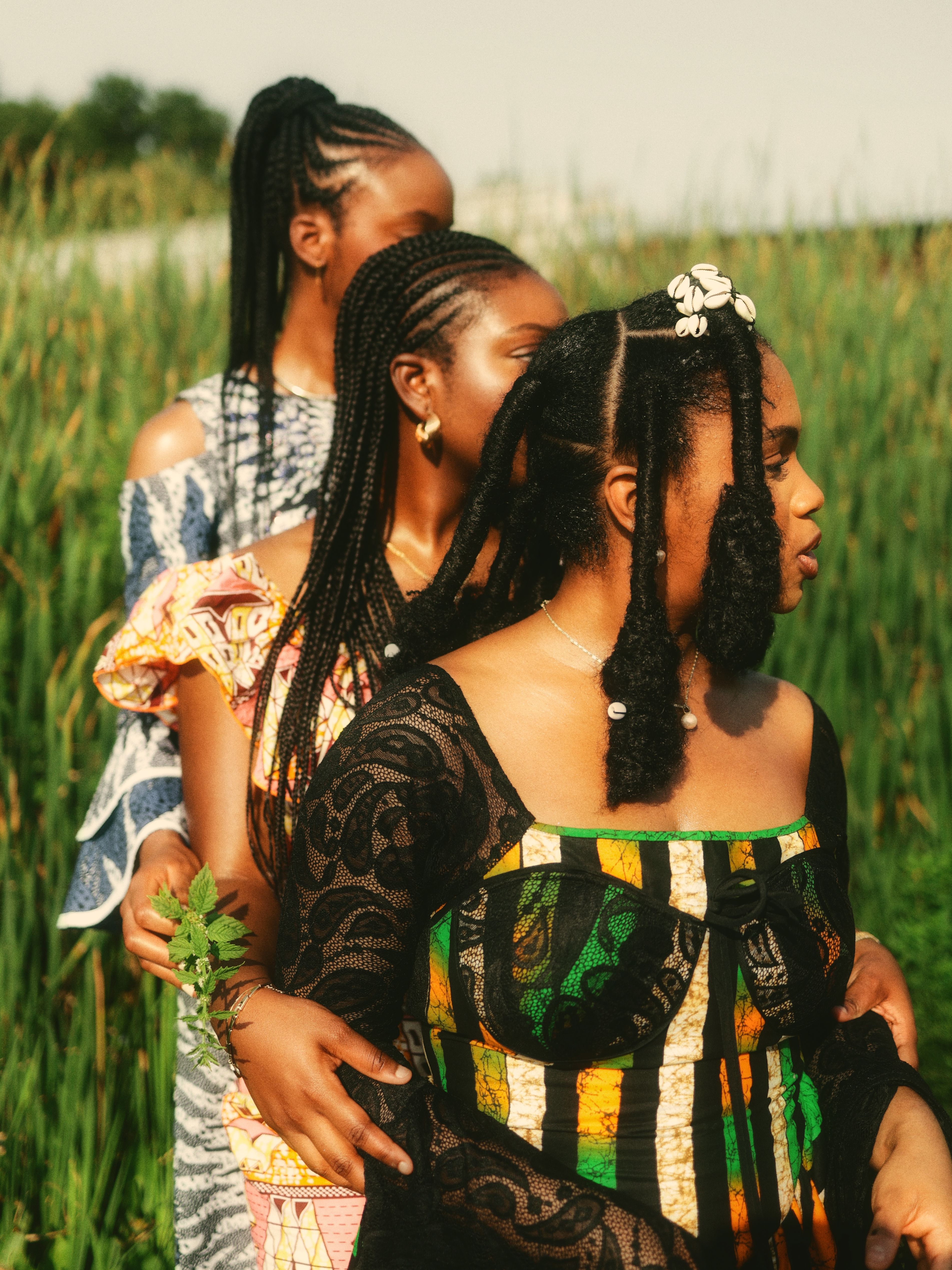 Three African women in colorful traditional dresses stand gracefully outdoors in a field.
