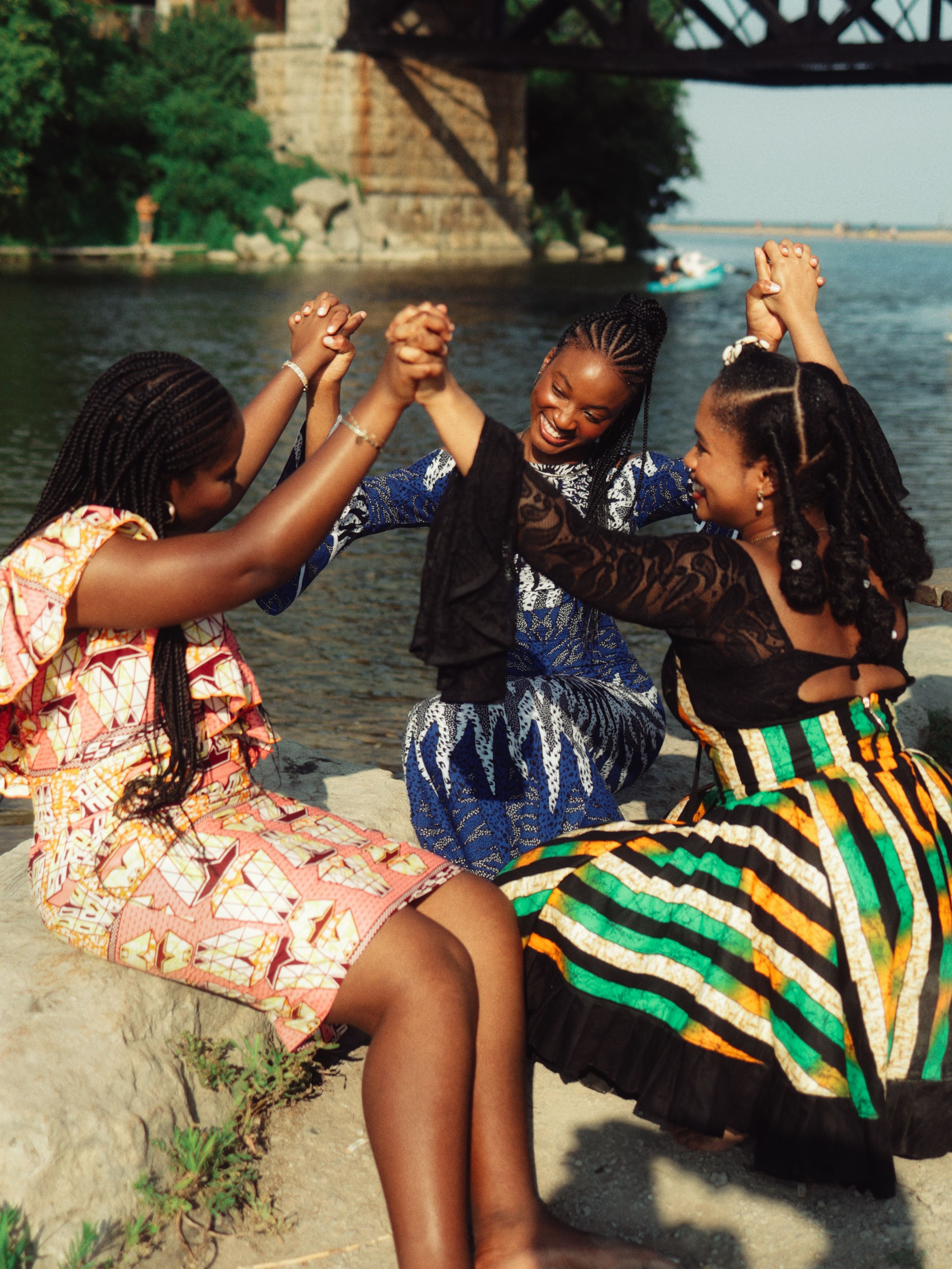 Three young women in vibrant dresses enjoying a sunny day by the river.