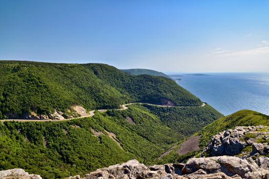 Breathtaking view of the Cabot Trail winding through lush hills and coastal cliffs in Nova Scotia.