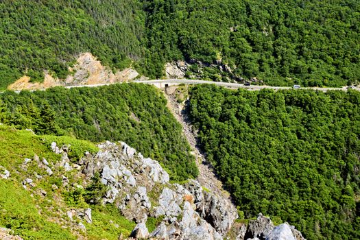 Aerial view of a road winding through the lush green Cape Breton Highlands in Nova Scotia, Canada.