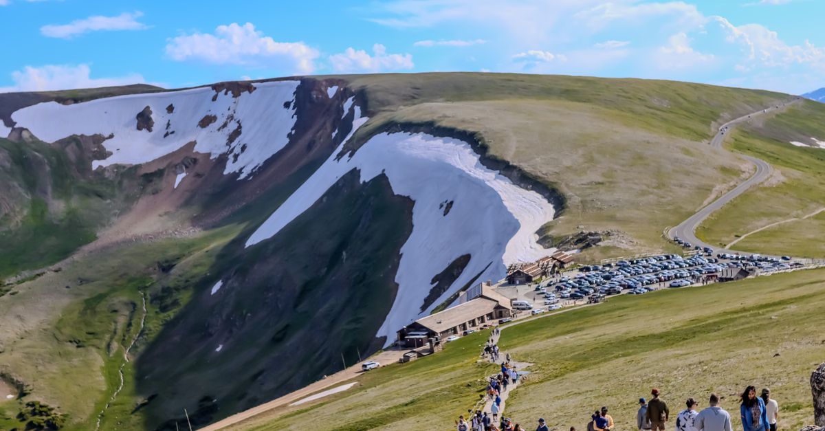 A scenic view of hikers exploring the Rocky Mountains with lush green terrain under a clear sky.
