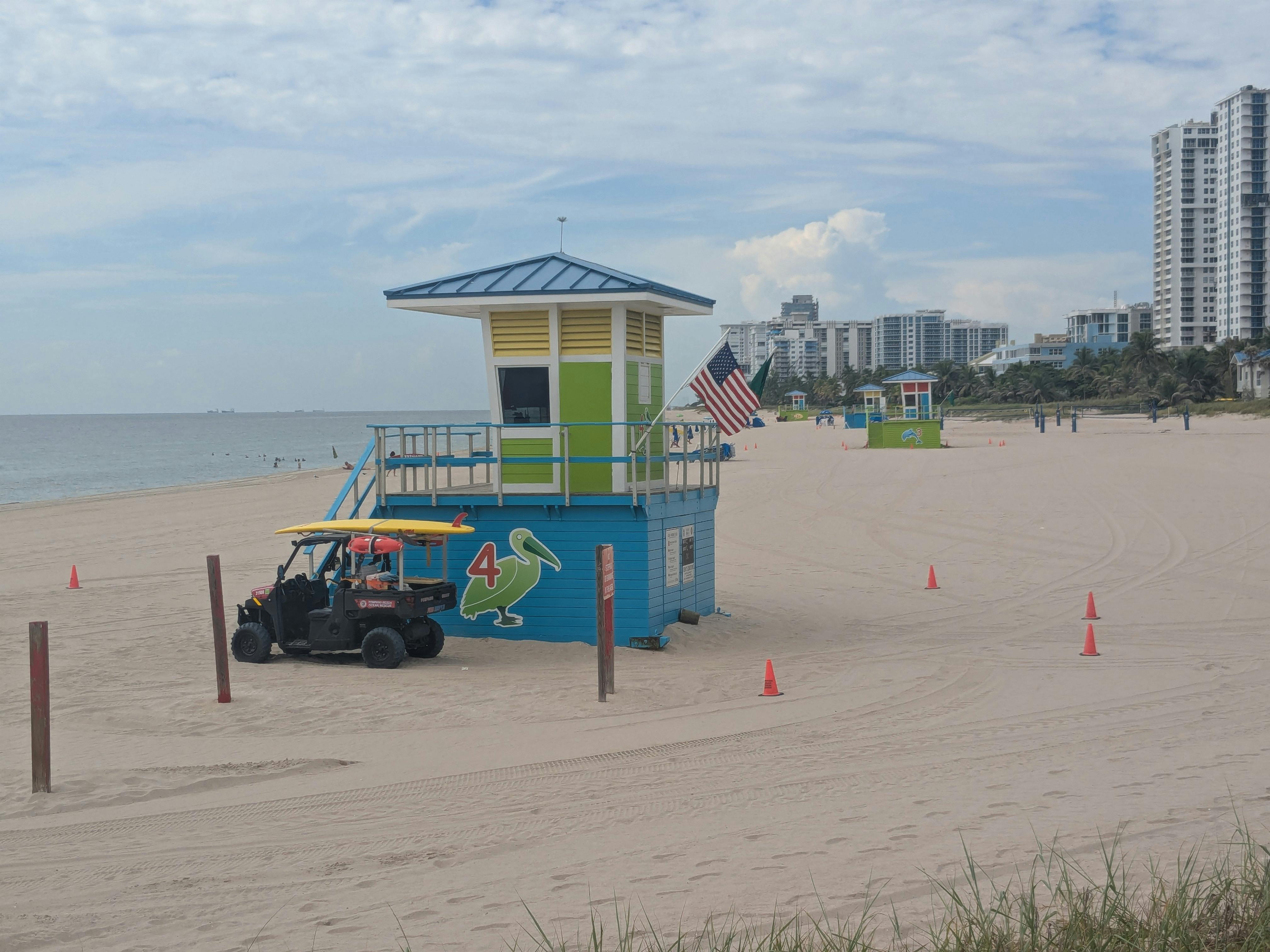 A vibrant lifeguard tower on Pompano Beach, Florida with a clear view of the ocean and nearby buildings in the background.