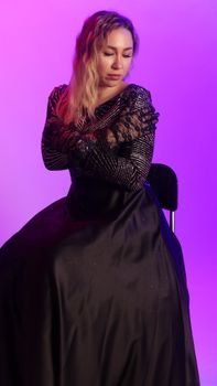 A woman in a stunning evening gown sitting against a purple background, exuding elegance.