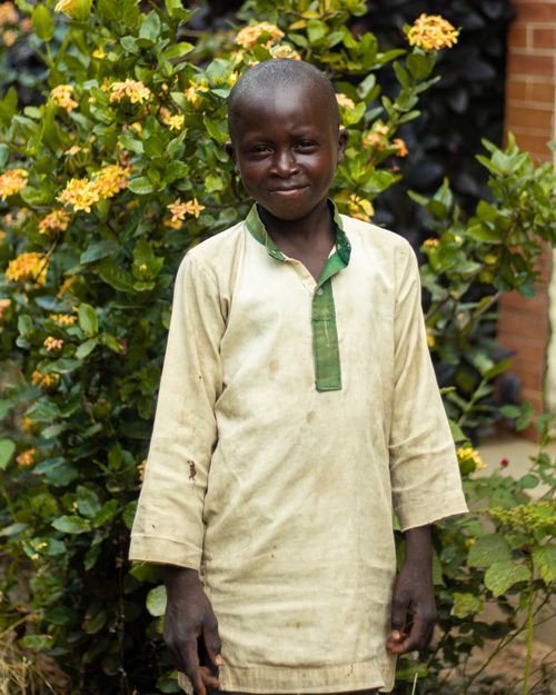 Free Portrait of a young boy smiling in a garden with yellow flowers, conveying joy and nature's beauty. Stock Photo