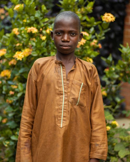 Free Boy in traditional dress standing outdoors with colorful flowers in the background. Stock Photo