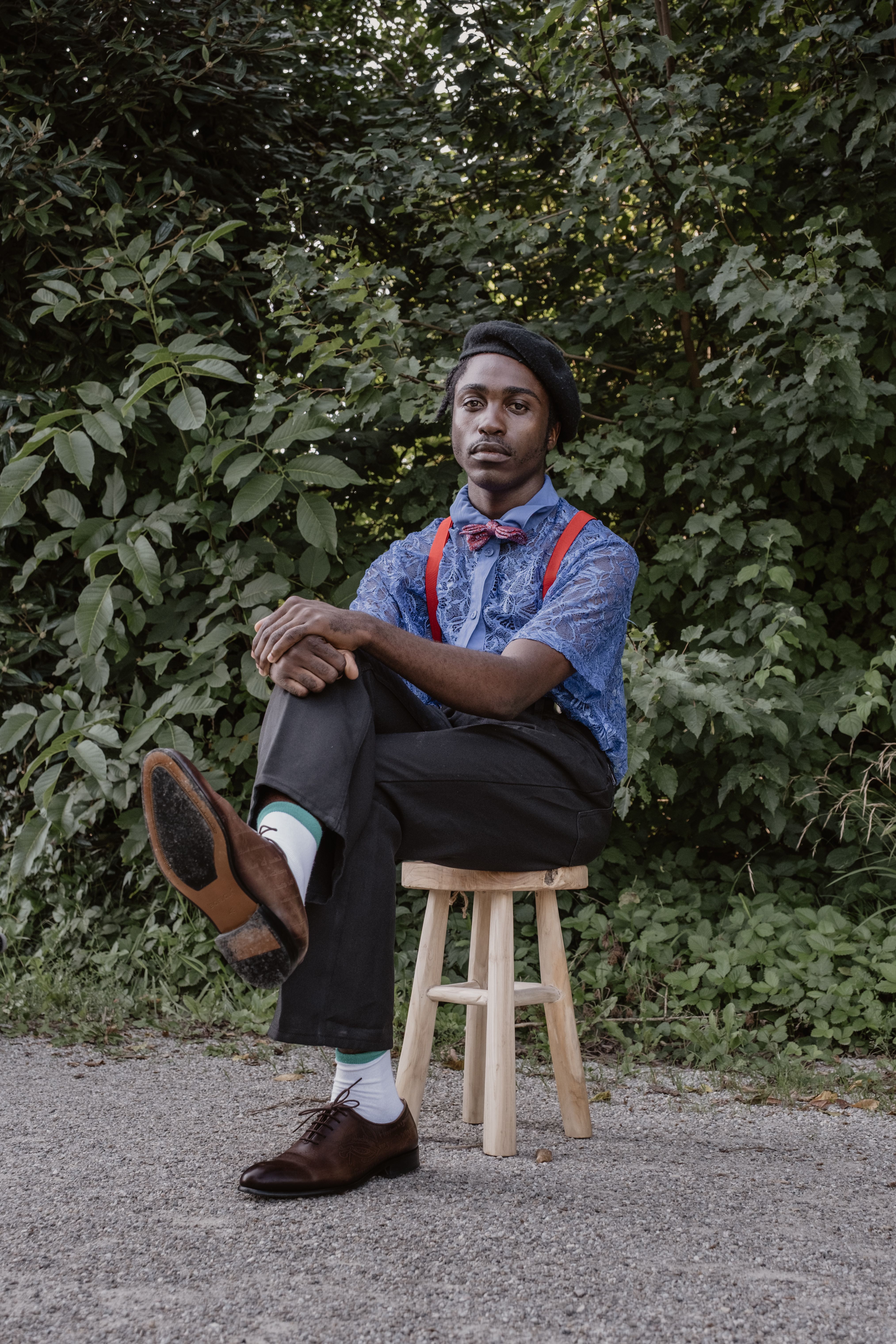 Elegant man in vintage attire seated outdoors in Munich, surrounded by lush greenery.