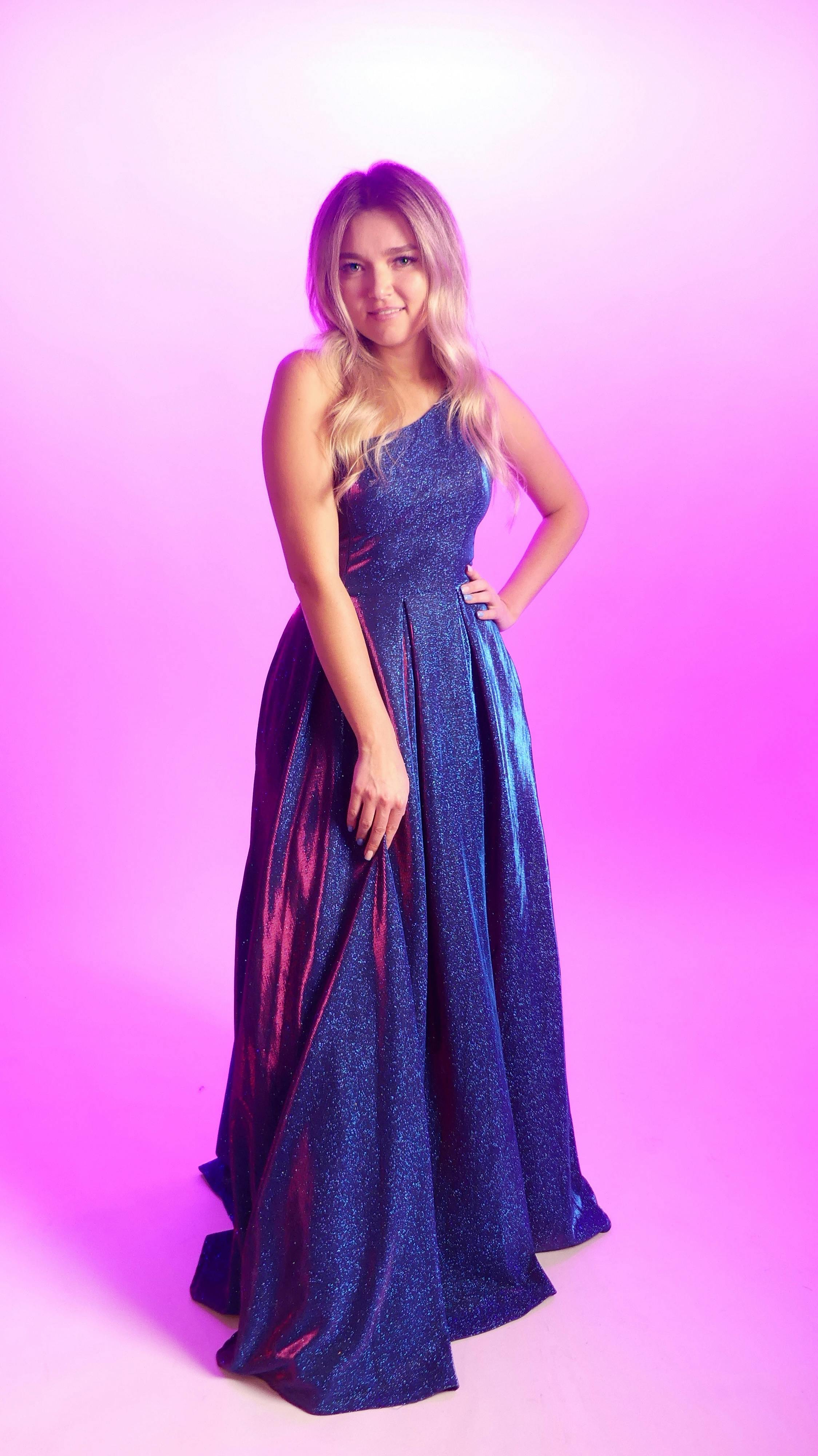Woman in a stylish blue gown posing confidently with a vibrant pink background.
