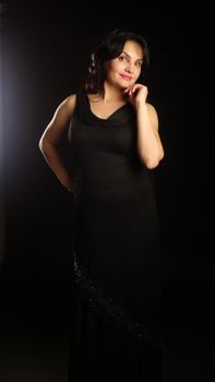 Graceful woman in a black evening gown posing with confidence in studio lighting.