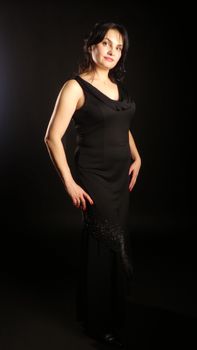 Stylish adult woman in a black evening dress posing in a studio setting.