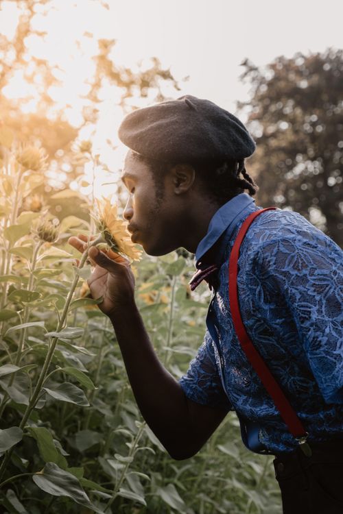 Free A man in stylish attire smelling sunflowers in a sunlit Munich garden. Stock Photo
