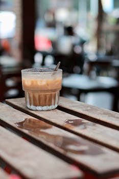 Close-up of iced coffee in glass on rustic wooden table in cozy cafe setting.