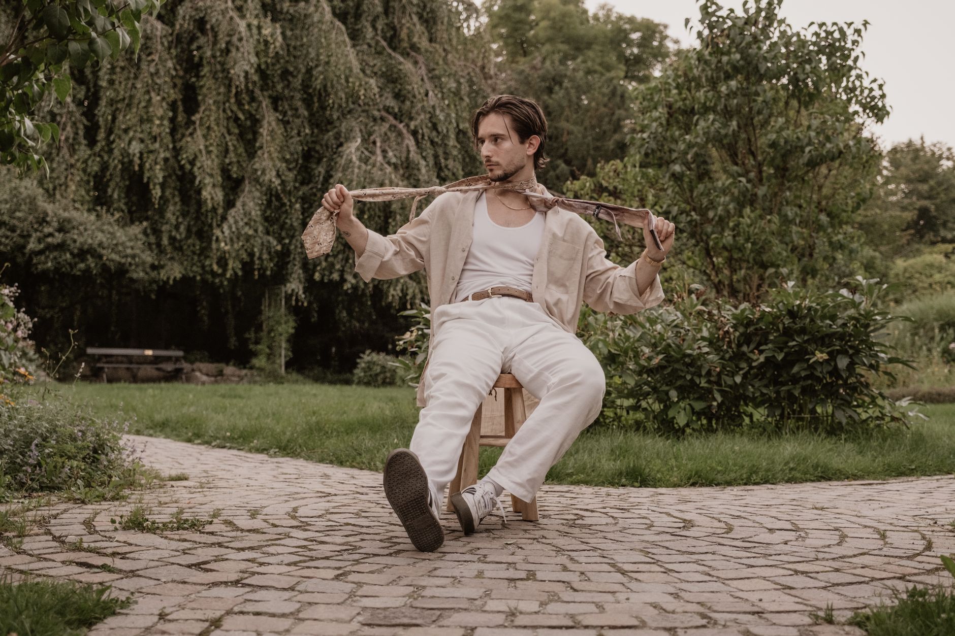 Trendy adult male showcasing modern vintage fashion in a lush outdoor garden in Munich, Germany.
