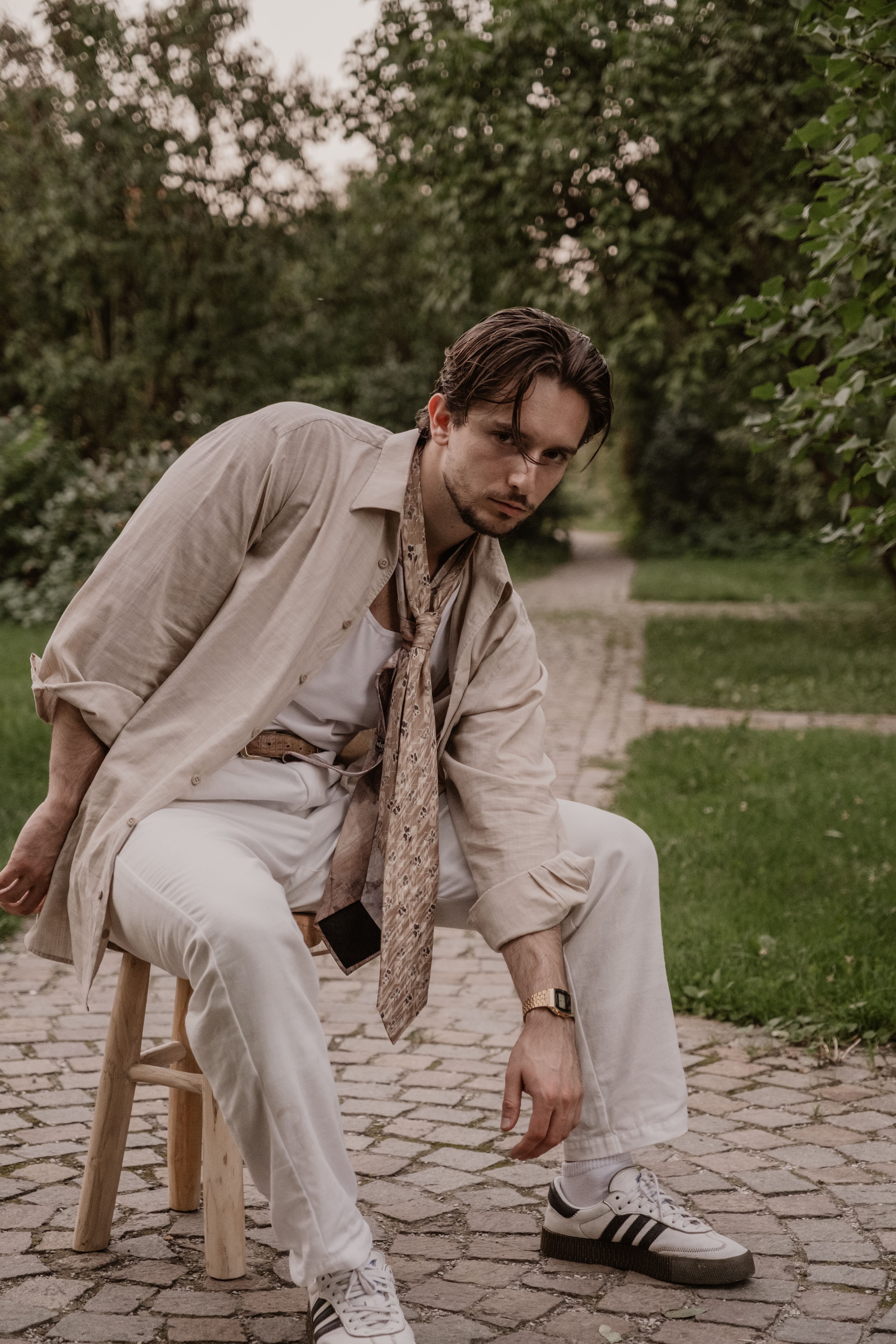 A fashionable man sitting on a stool, exuding 90s aesthetic in a park setting.