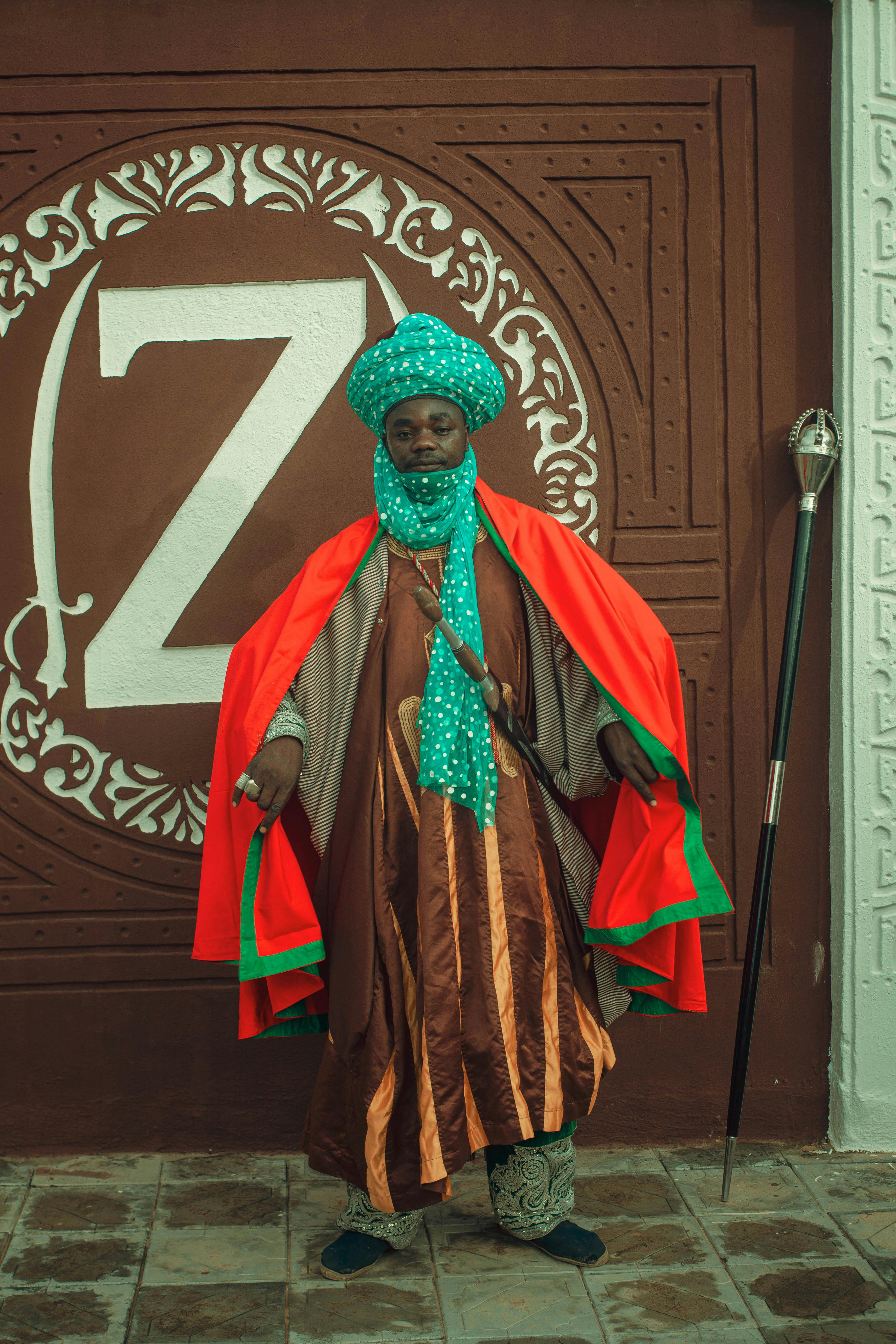 Portrait of a man in vibrant traditional attire against an ornate wall with 'Z' emblem.