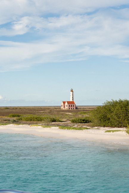 Serene view of Klein Curaçao island's lighthouse and sandy beach under a blue sky.