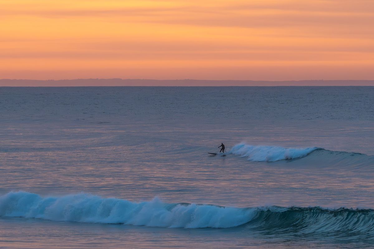 Lone surfer paddling out to catch waves at dawn during golden sunrise light