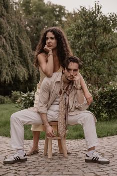 Stylish couple poses in vintage-inspired outfits in a lush garden setting.