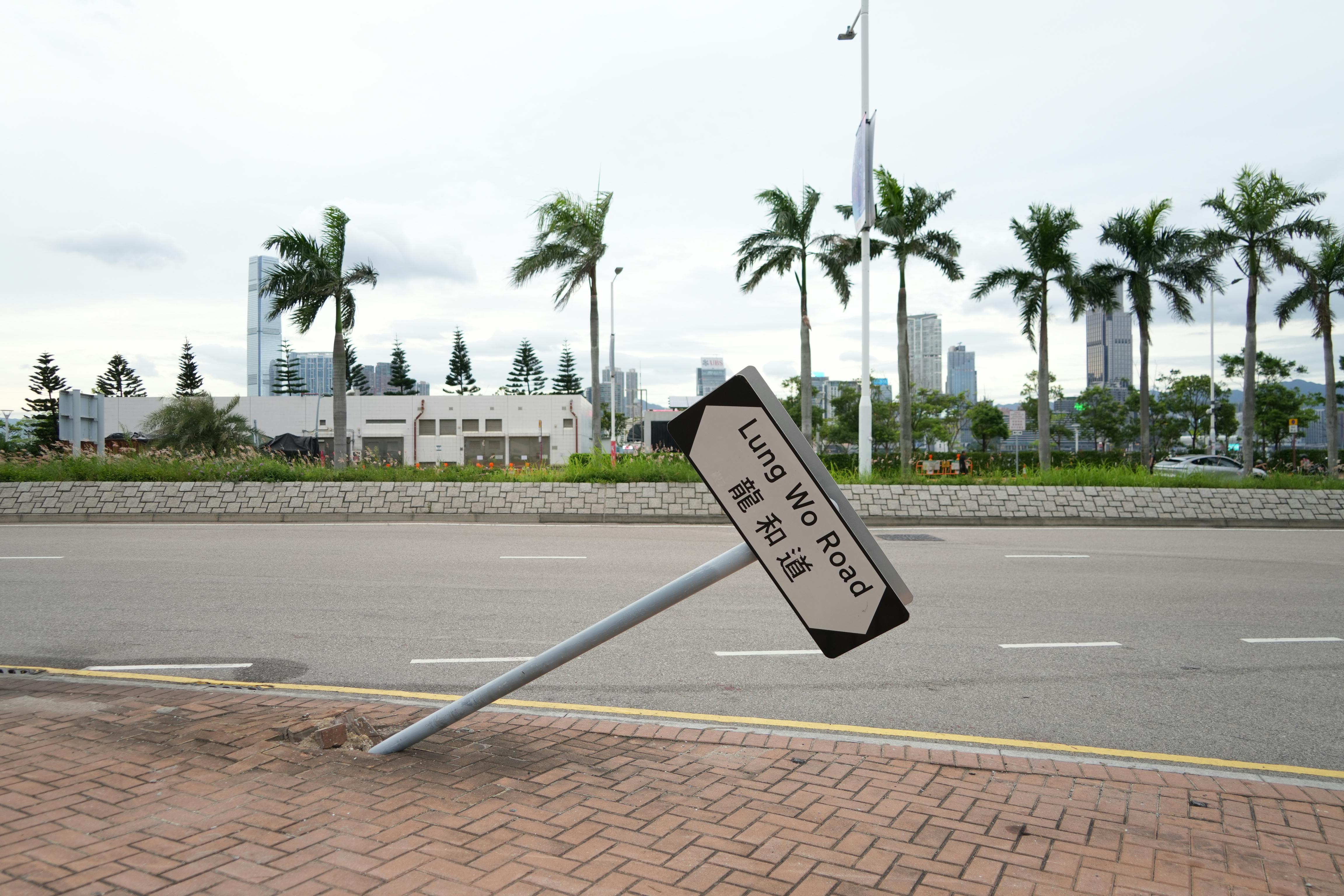 A tilted road sign at Lung Wo Road with a cityscape and palm trees in Hong Kong Island.