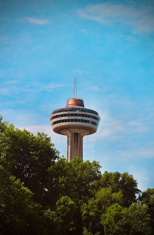 Free The Skylon Tower rises above lush green trees under a clear blue sky in Niagara Falls, Canada. Stock Photo