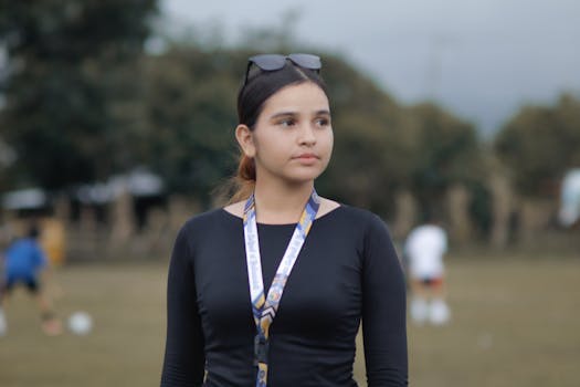 A young woman in casual clothing with sunglasses and a lanyard, outdoors.