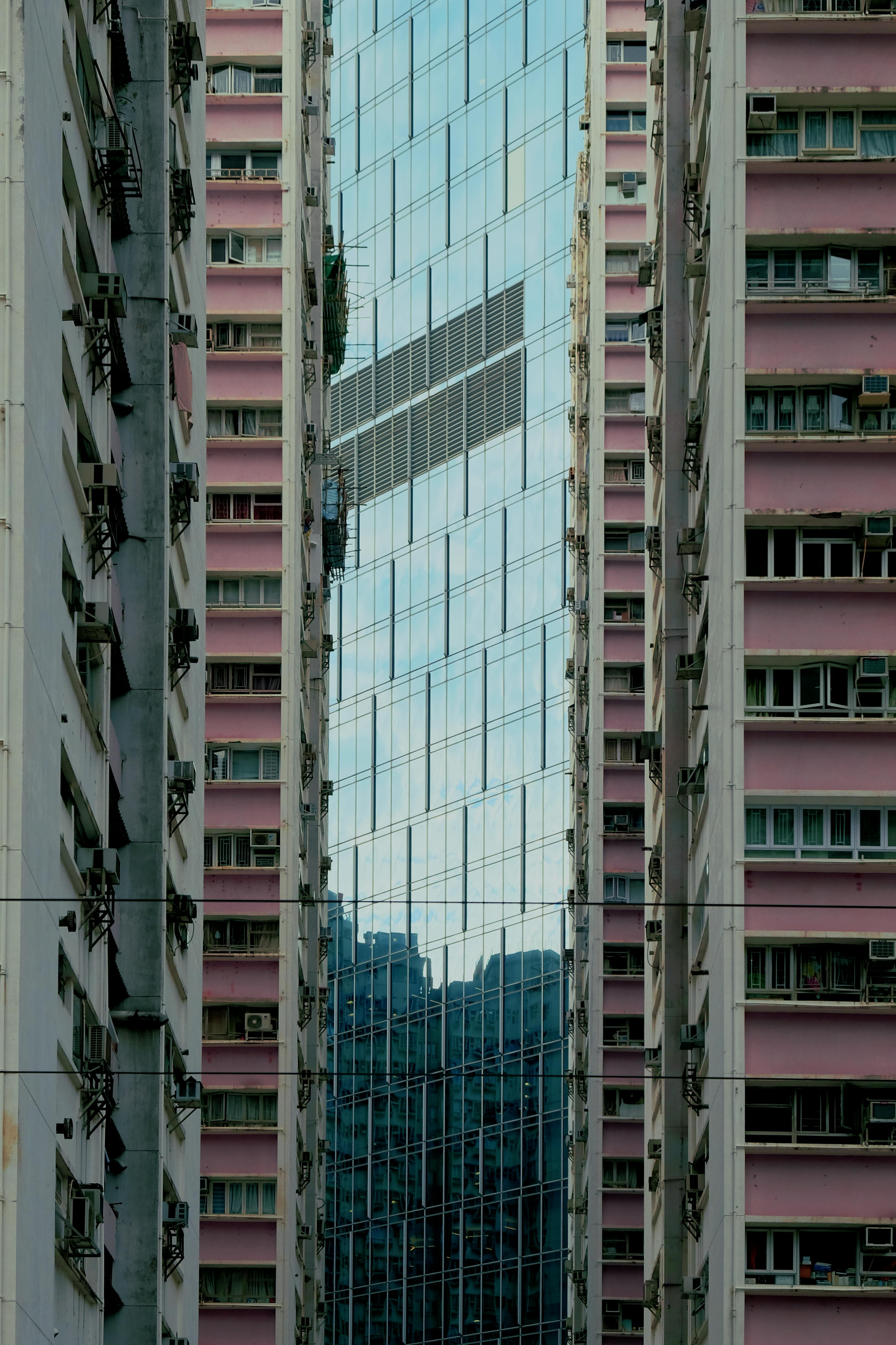 Modern glass skyscraper flanked by urban buildings, showcasing reflection and geometry.