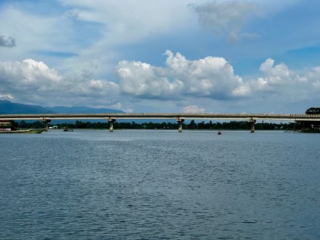 Peaceful river scene with a bridge under a cloudy blue sky, ideal for travel and nature themes.