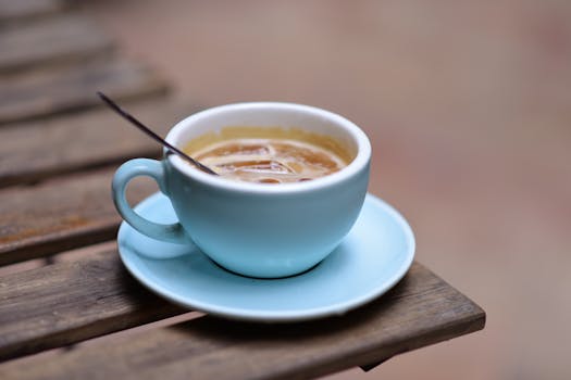 Close-up of a steaming coffee in a blue cup on a wooden table outdoors.