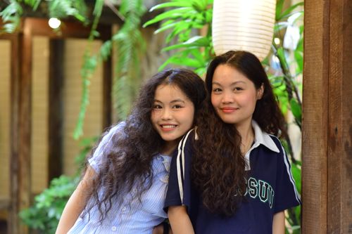 Free Two young women happily pose together in an indoor setting surrounded by greenery. Stock Photo