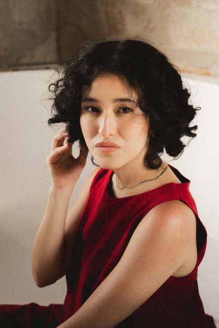 Elegant portrait of a woman in a red dress, set in a serene, soft-lit environment.