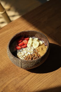 Healthy smoothie bowl topped with strawberries, bananas, oats, and peanut butter in coconut shell.