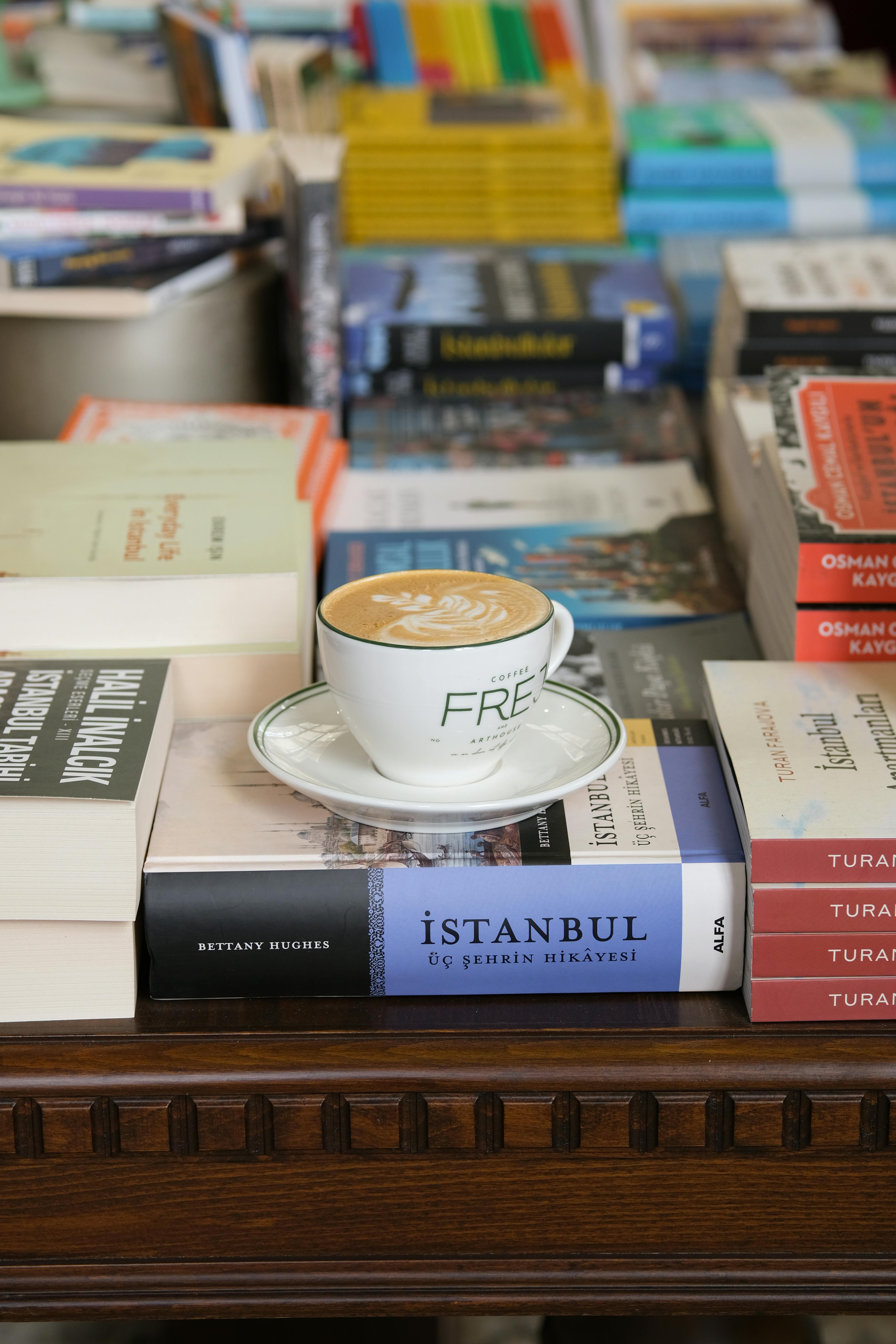 A cup of cappuccino with intricate latte art sitting on a stack of books in a library setting.