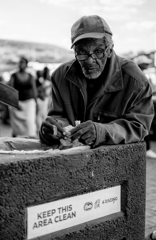 Free Black and white portrait of an elderly man leaning on a trash bin in Johannesburg, advocating cleanliness. Stock Photo