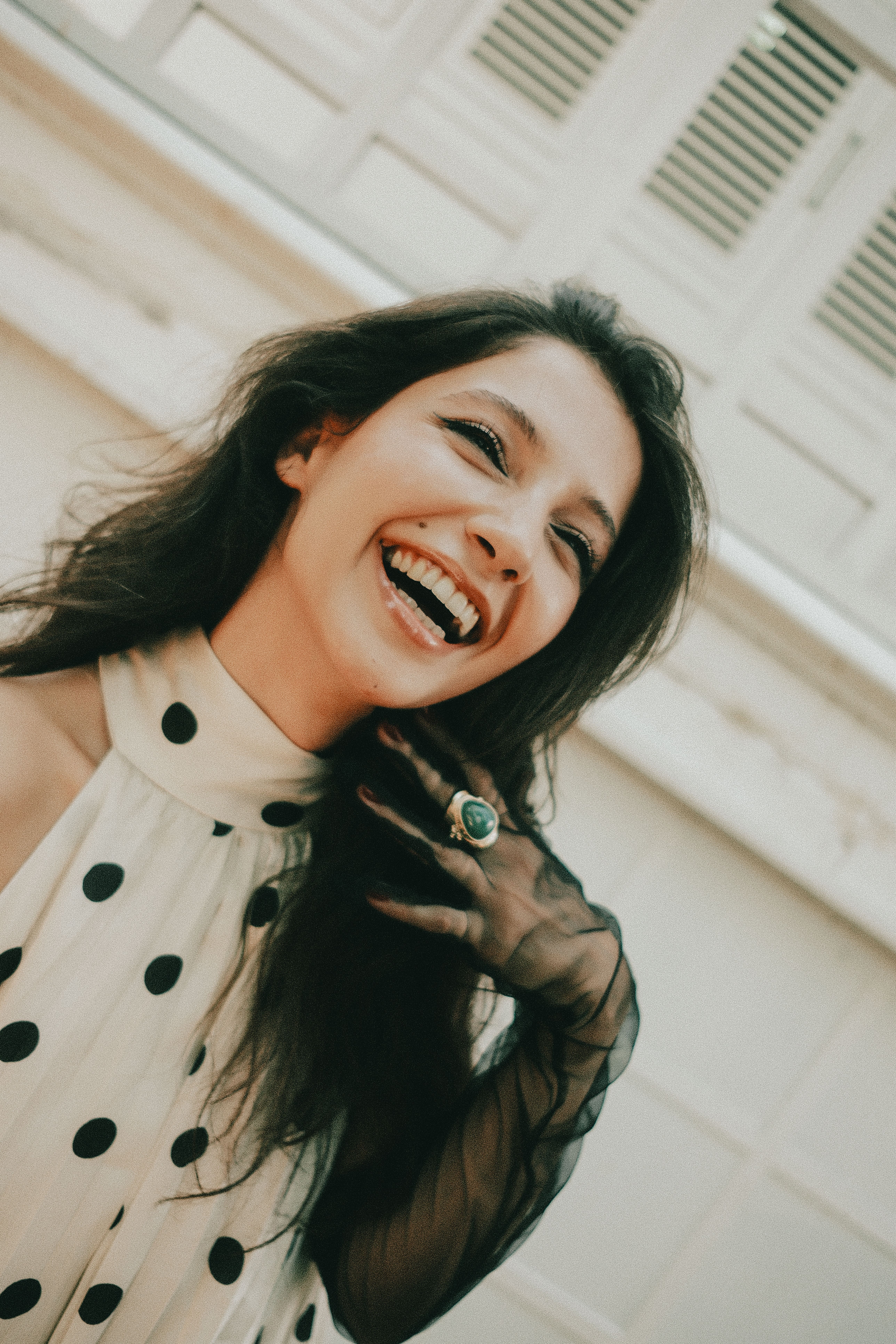 Woman in polka dot dress laughing joyfully outdoors, capturing happiness and style.