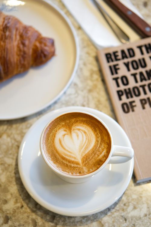 Free A cappuccino with heart-shaped latte art next to a croissant on a table. Stock Photo