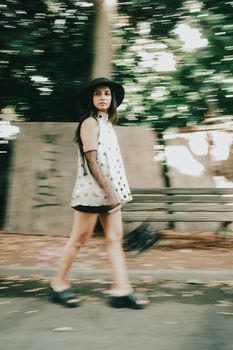 Artistic motion blur of a woman walking in a park, wearing a hat and dress, evokes urban lifestyle.