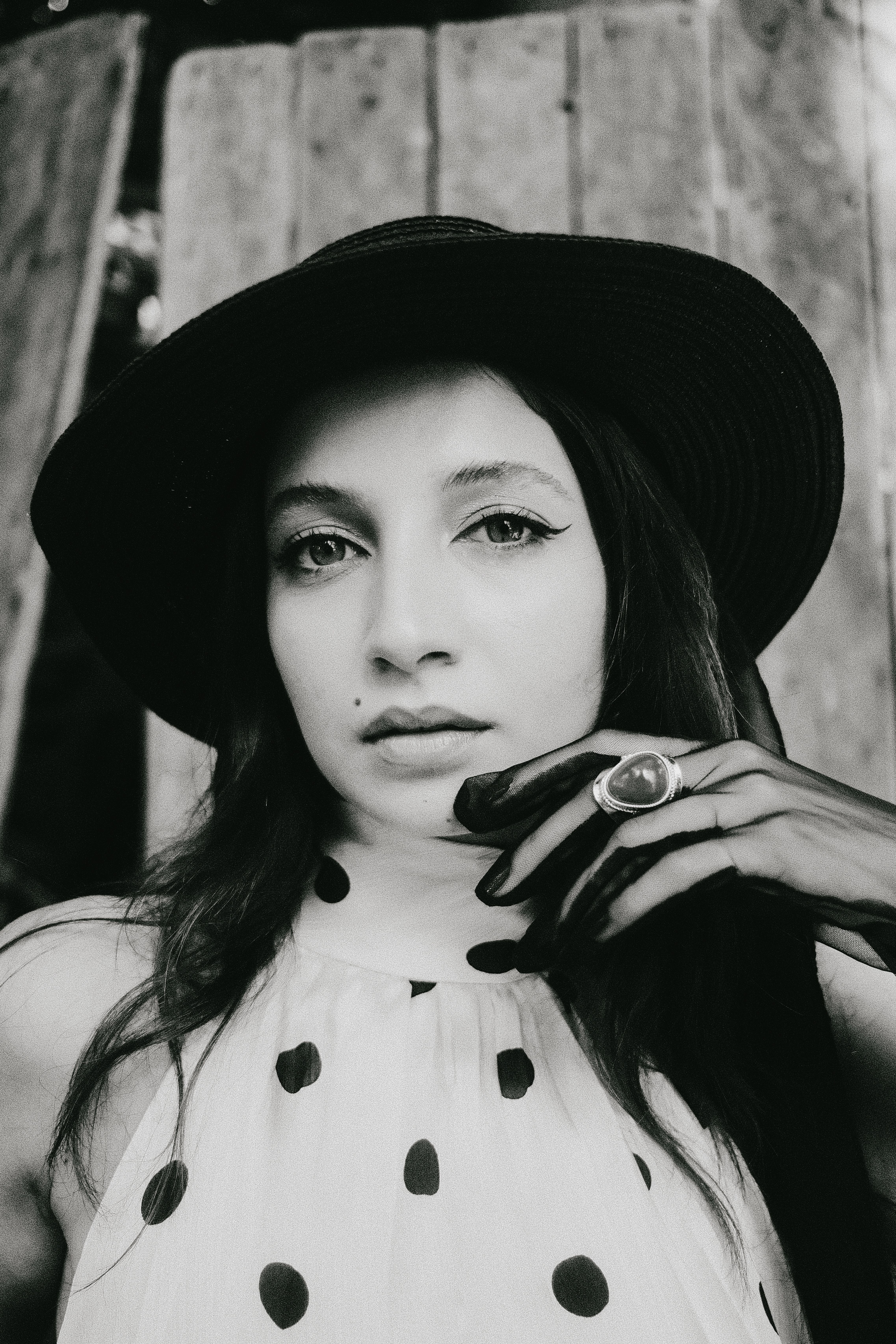Black and white portrait of a woman in a polka dot dress with a black hat and gloves.