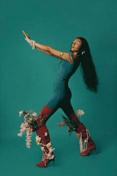 Captivating portrait of a model in vibrant fashion with floral-embellished boots against a teal background.