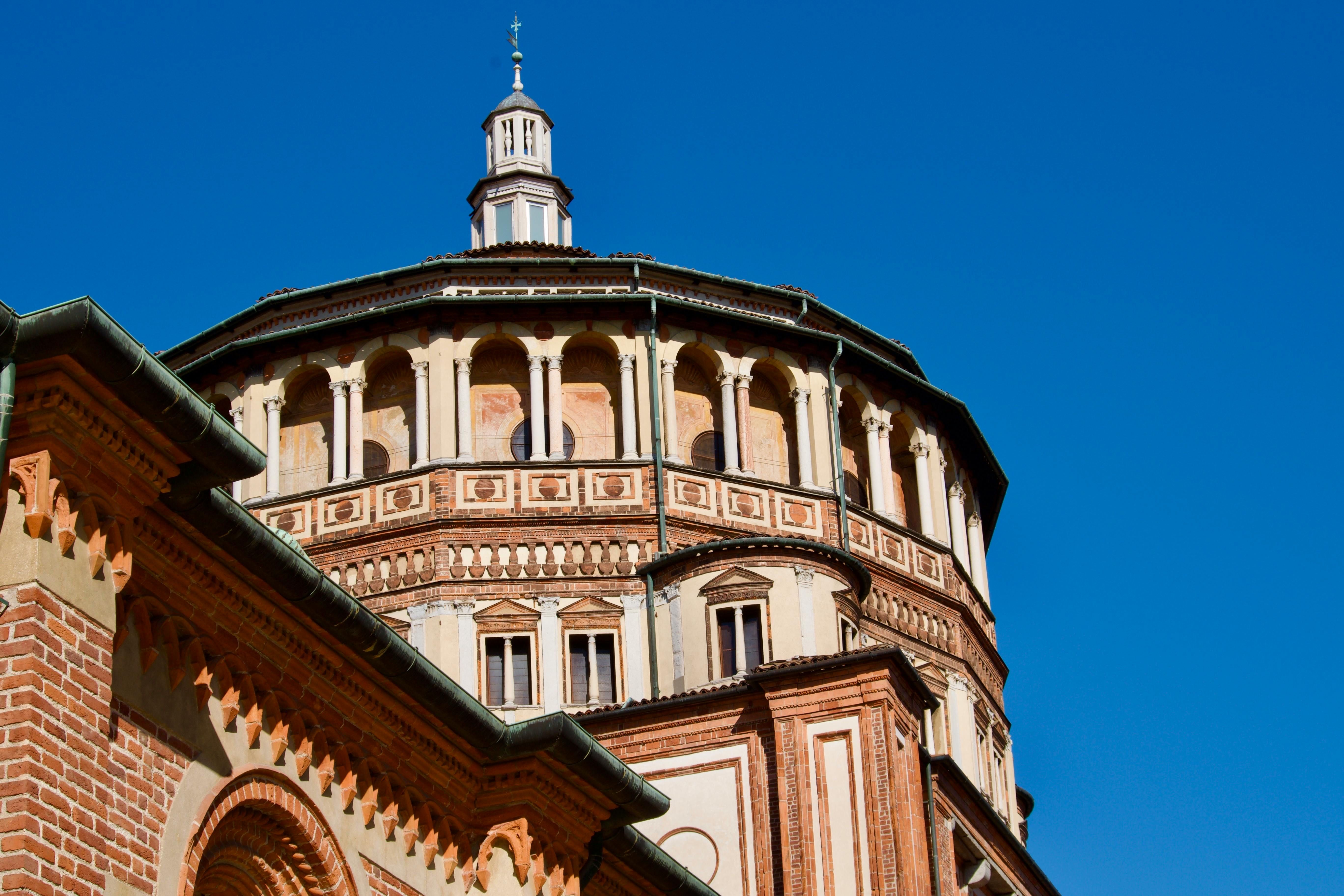 Ápside de tijolos iluminada pelo sol e cúpula renascentista da Igreja de Santa Maria delle Grazie em Milão, Itália, sob um céu azul límpido, sem pessoas
