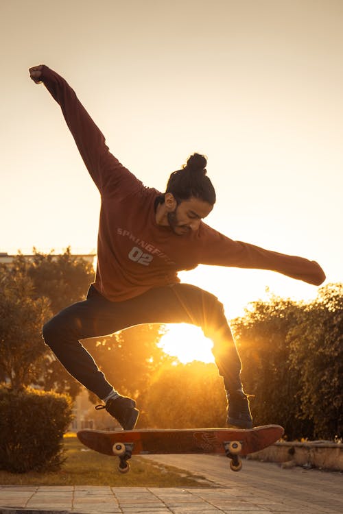 太陽光線穿過穿著紅色圓領長袖襯衫滑板的男人