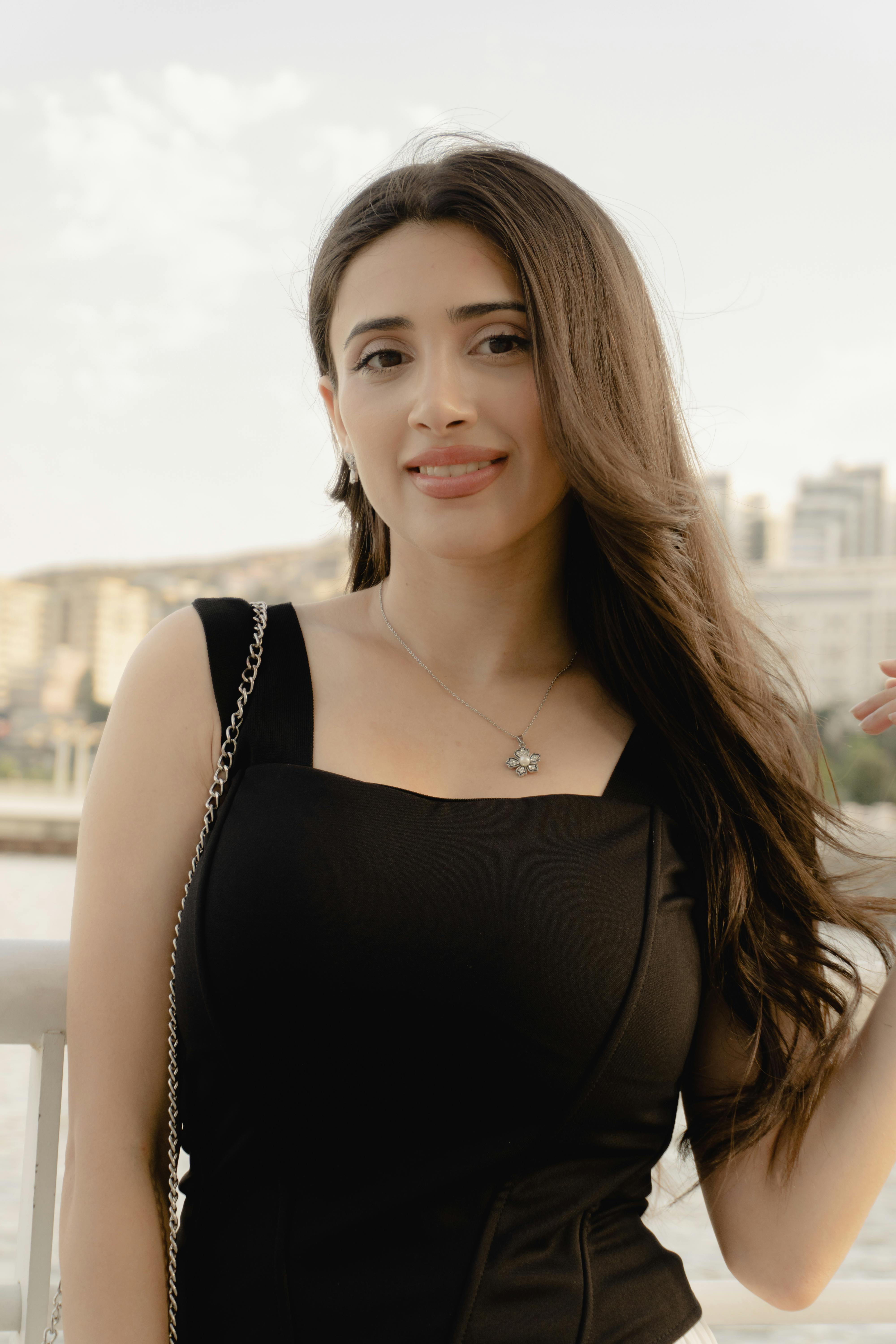 Elegant woman in a black dress posing by the waterfront in Baku, capturing urban sophistication.