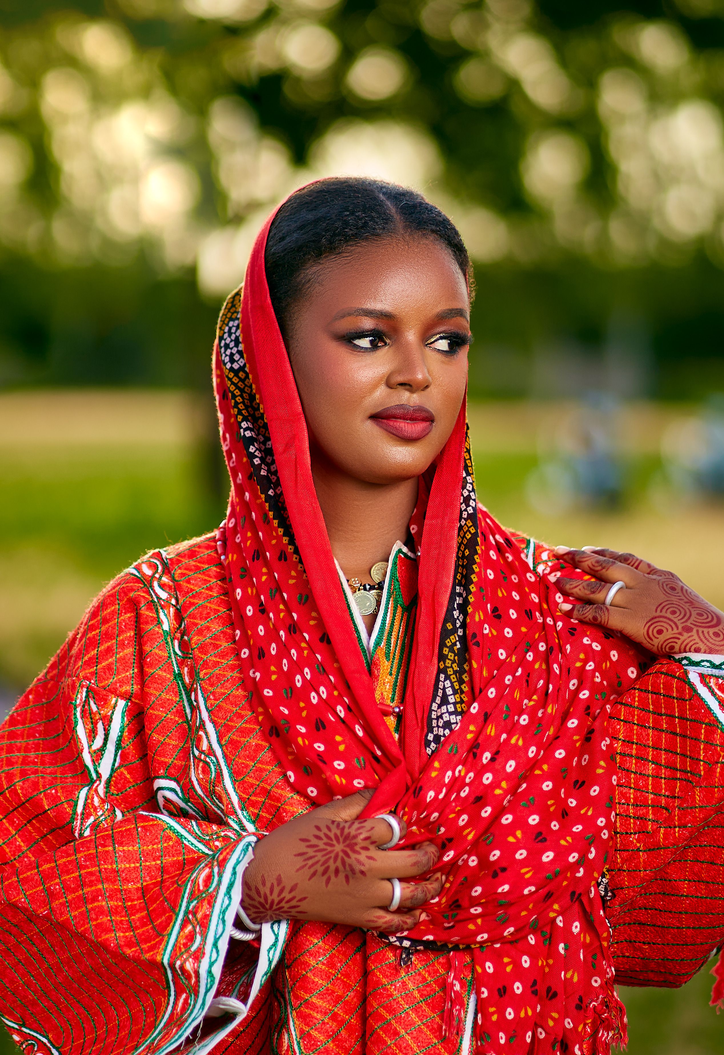 Portrait of a stylish woman in vibrant red traditional clothing with intricate patterns outdoors.