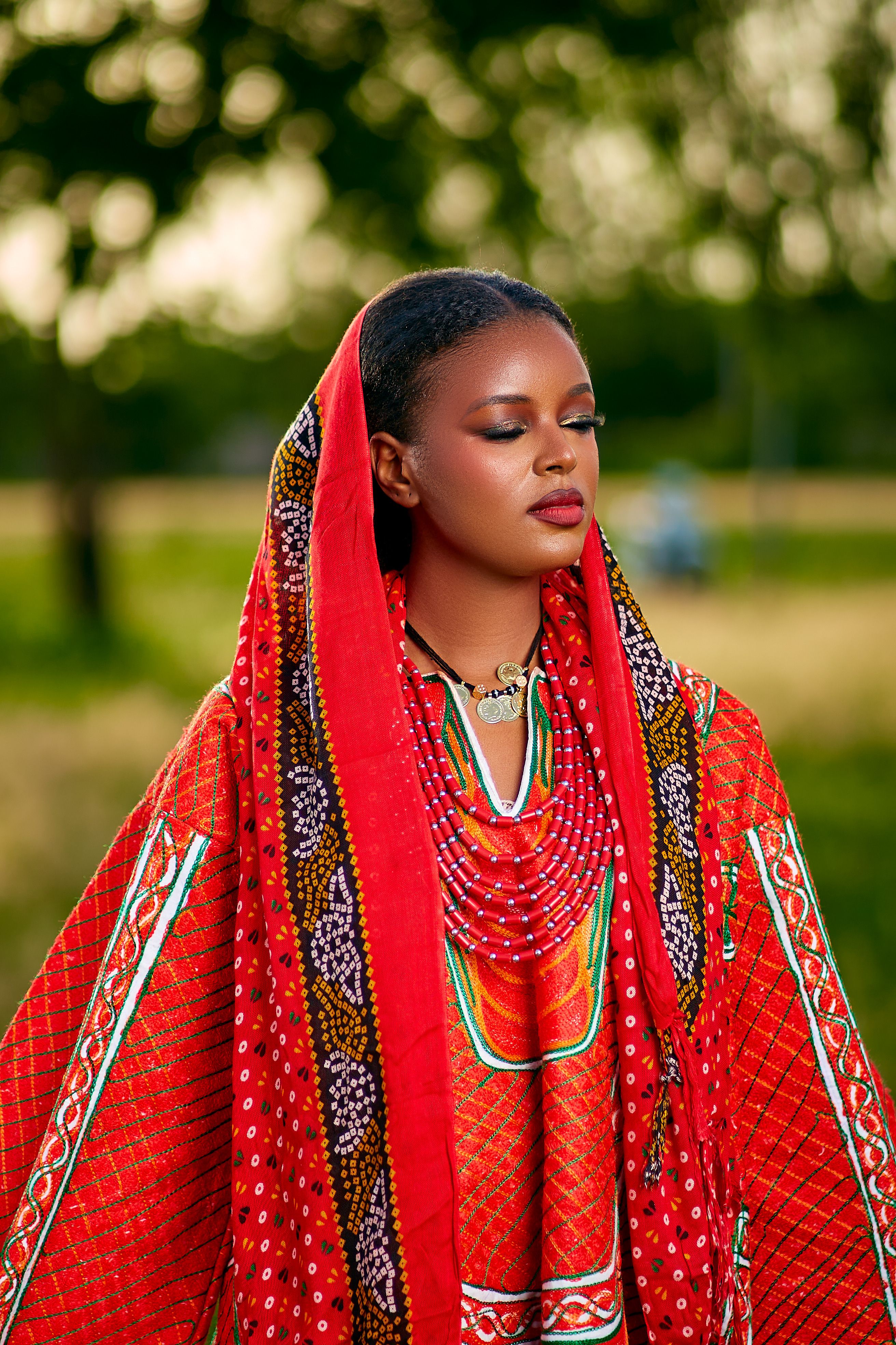 Portrait of a woman in vibrant African attire with closed eyes, outdoors in nature.