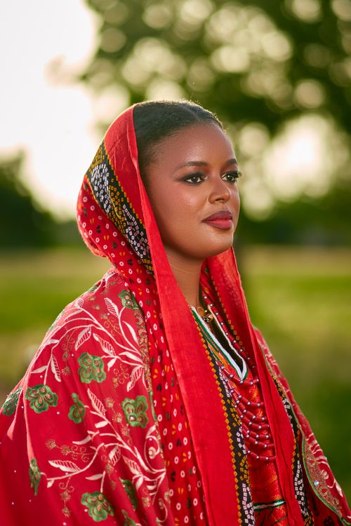 Free A woman in vibrant red traditional clothing stands outdoors, exuding grace and confidence. Stock Photo