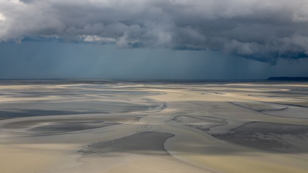 Moody clouds cast shadows over the sweeping sands of Normandy's coastal landscape.