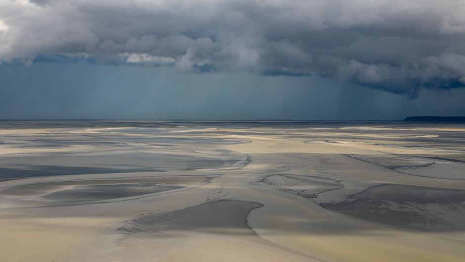 Moody clouds cast shadows over the sweeping sands of Normandy's coastal landscape.