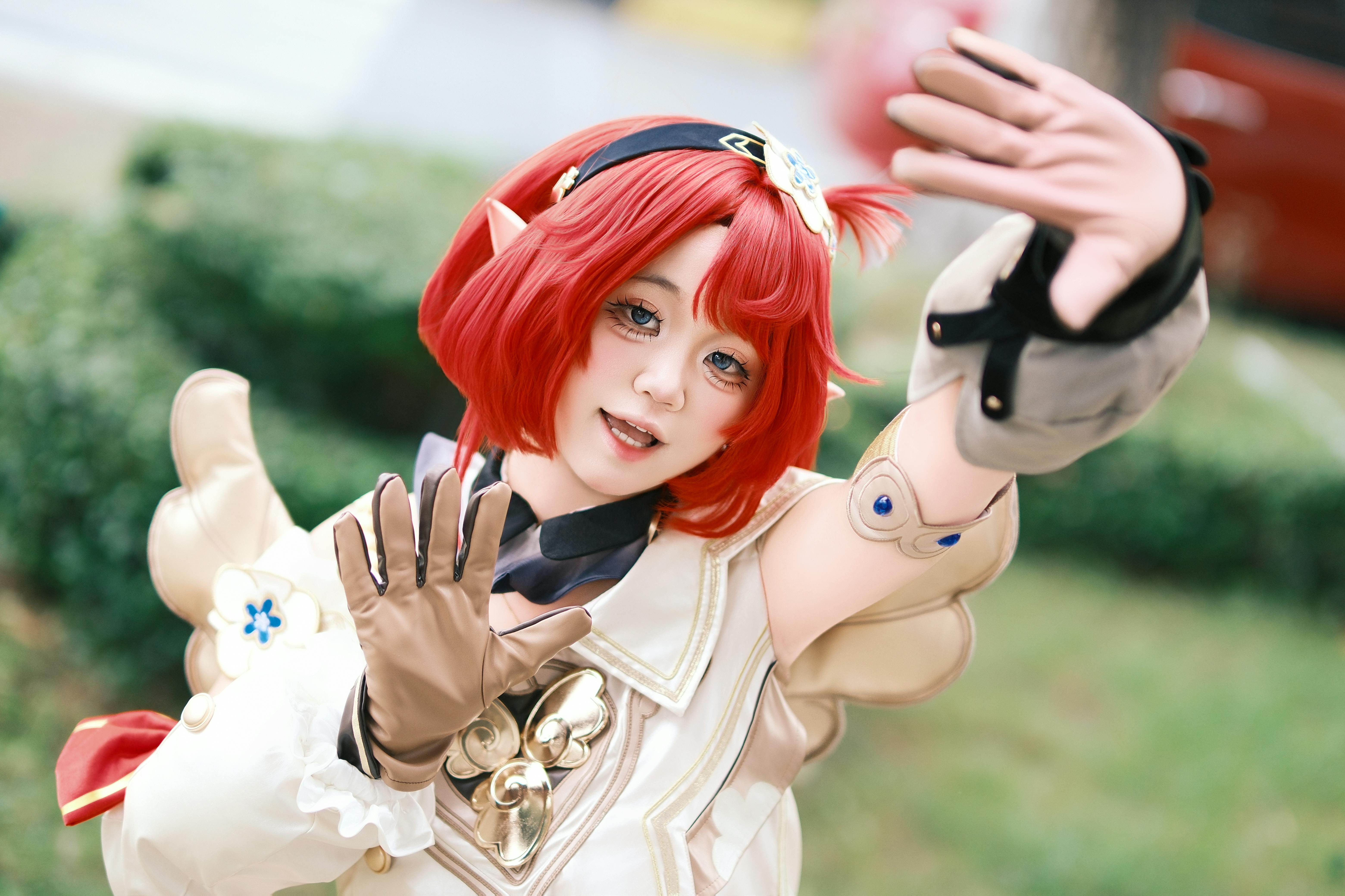 Dynamic cosplay photo of a young woman with red hair and elf ears outdoors.