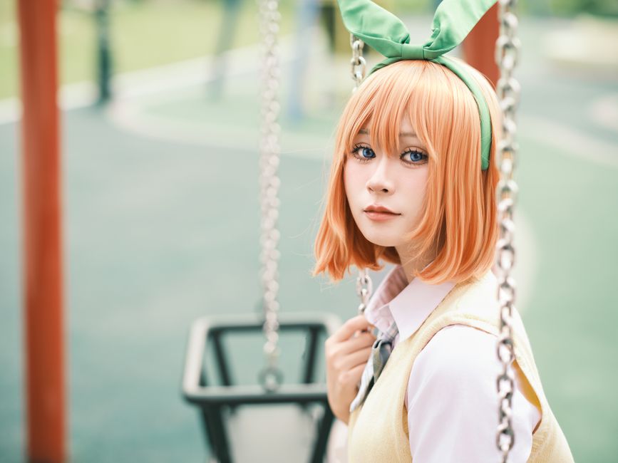 Cosplayer dressed in vibrant costume poses on a playground swing.