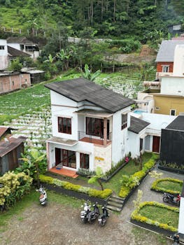 A modern two-story house with a lush garden and rural surroundings.